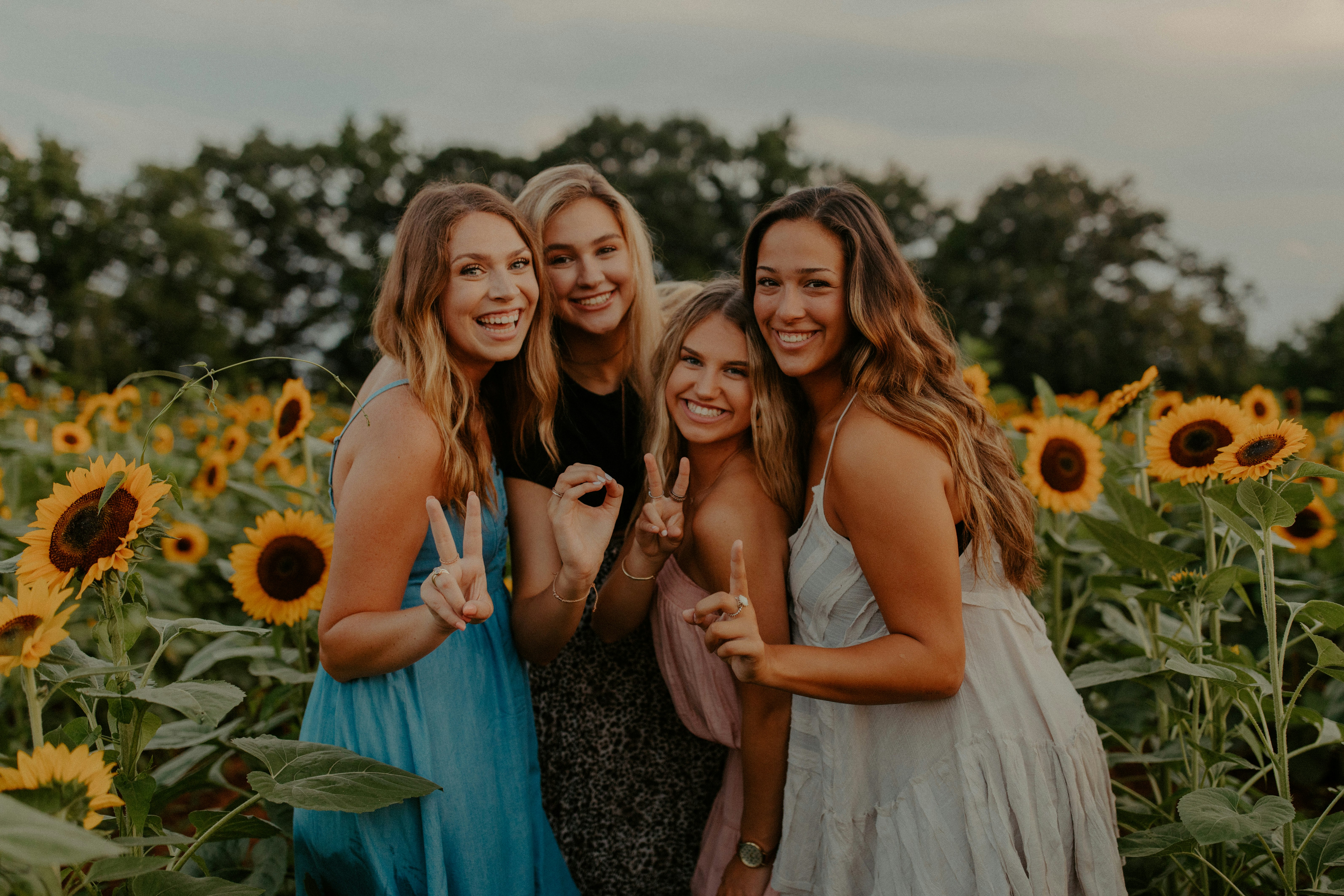 3 women smiling and standing on sunflower field during daytime